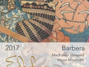 Edaphos Madhavan Vineyard Barbera 2018 label; A rectangular label with ornate abstract design with mixed patterned fabrics in blues, beige, cream and black. The bottom third is overlaid by a transparent white label with gold and black text