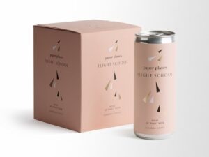 Paper Planes "Flight School" Canned Pinot Noir (4 x 250ml); A white square label showing a box, and one can of wine. Both the box and can are pale pink, with small black, gold and white triangles scattered about.