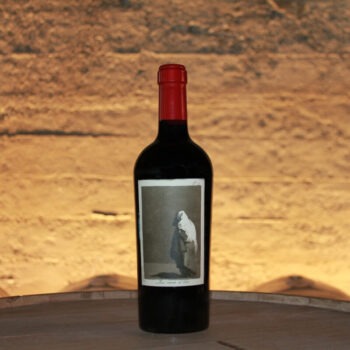 el Coco 2019; An oblong label showing a bottle of wine standing on a barrel top in the foreground, with more barrels beyond, against a sun kissed brick wall